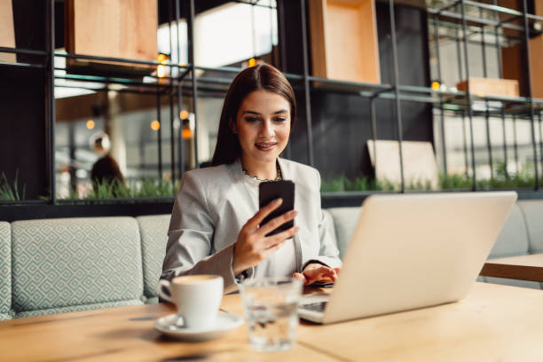istock Beautiful brunette is using her phone while sitting in cafe in front of a laptop 956321534