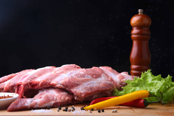 istock Raw Ribs on a rustic cutting board with salt, pepper and grinder for spices . Black Background for copy space. Top View. 956321760
