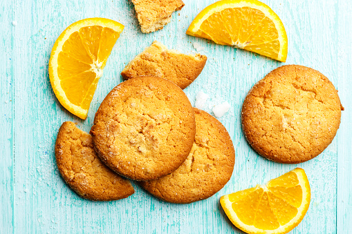 homemade cookies and chopped oranges on a blue wooden background, space for text