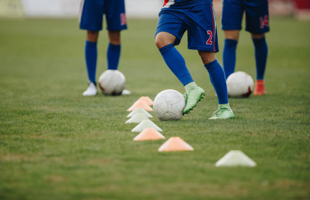 Unrecognizable soccer players exercising dribbling among cones on a sports training.