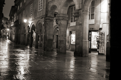 Santiago de Compostela, Spain- December 13, 2017: Street view in old town Santiago de Compostela (Galicia, Spain)  rainy night, stone arches, black and white view,  reflections on wet stone flooring.