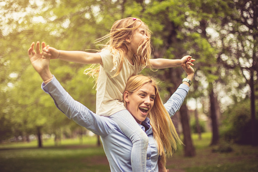 Mother carrying daughter on shoulders and spending time in park.