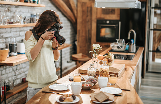 Young female photographer taking photos of breakfast table in the kitchen.