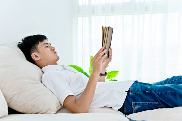 istock Young asian man reading a book at home 956337248