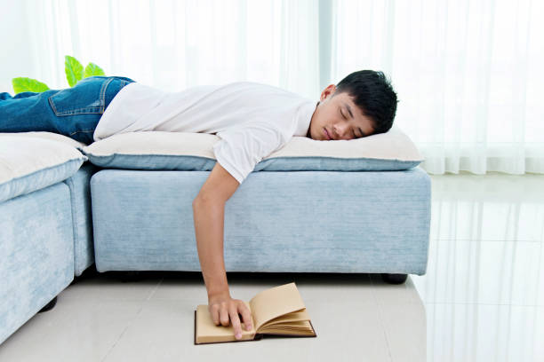 istock Young asian man with book asleep on sofa 956337520