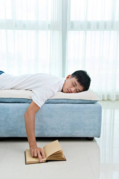 istock Young asian man with book asleep on sofa 956337578