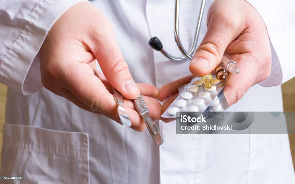 Concept photo choice or strategy for treating patient - surgical (operation) or therapeutic (with medications). Doctor holds surgical scalpels in one hand, in another - pills in blisters and ampoules Abortion Stock Photo