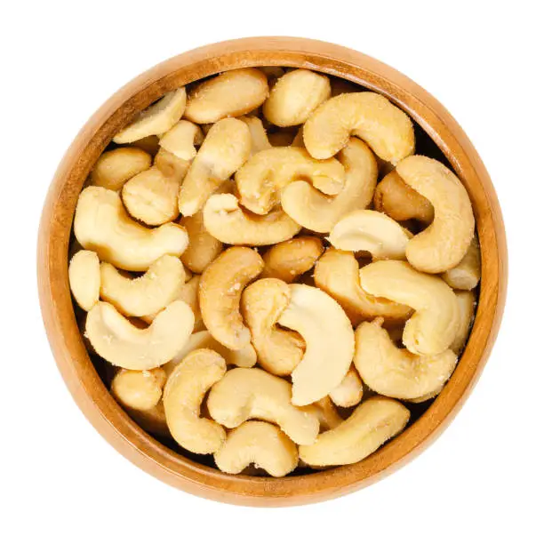 Roasted salted whole cashews in wooden bowl. Light brown nuts, used as a snack. Seeds of Anacardium occidentale. Isolated macro food photo close up from above on white background.