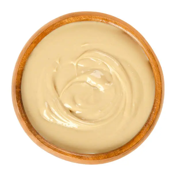 Cashew butter in wooden bowl. Food spread made from roasted cashews. Light brown, smooth food paste. Cream of nuts of Anacardium occidentale. Isolated macro food photo close up from above over white.