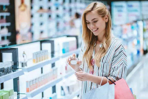 Attractive young girl is doing shopping with shopping bags in perfume store in modern mall.