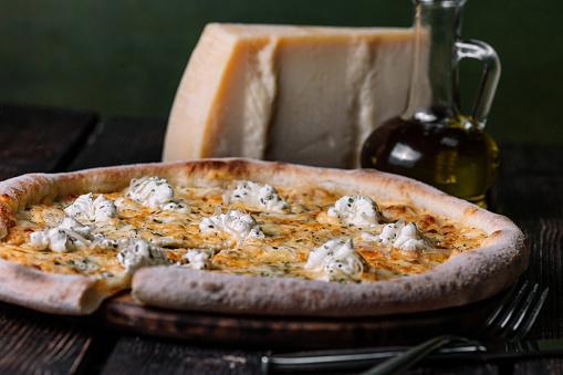 Quattro formaggi pizza with bottle of olive oil and parmesan on the cutting board on dark wood background