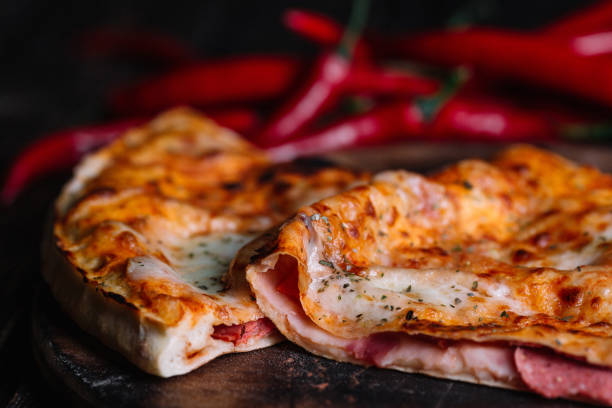 istock Cutted Spicy Calzone - Stuffed Pizza with chilli peppers on dark wood background 956346520