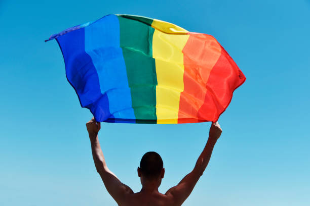 man with a rainbow flag over his head - gay pride flag gay pride gay man homosexual imagens e fotografias de stock