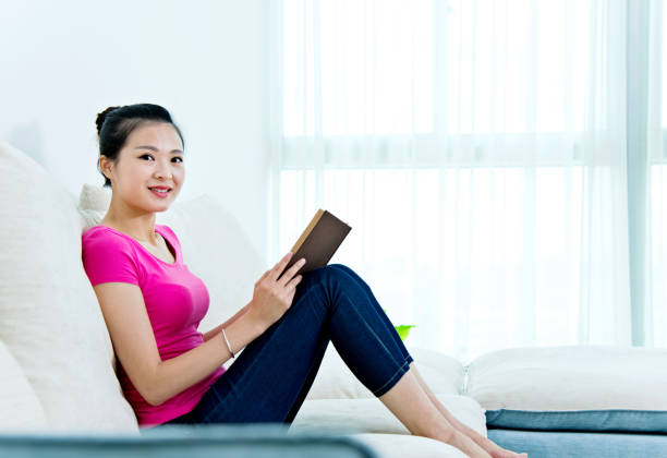istock Beautiful young woman reading a book at home 956356270