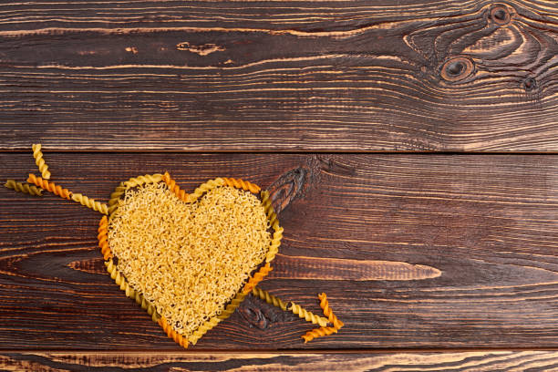 Valentines Day wooden background. Top view of heart with an arrow made of pasta and copy space.