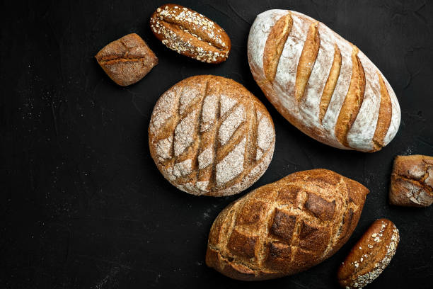 istock Bakery - gold rustic crusty loaves of bread and buns on black chalkboard background 956367936