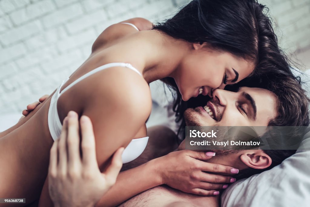 Young love couple in bed Happy couple is lying in bed together. Enjoying the company of each other. Couple - Relationship Stock Photo