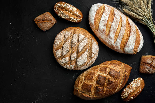 istock Bakery - gold rustic crusty loaves of bread and buns on black chalkboard background 956369912