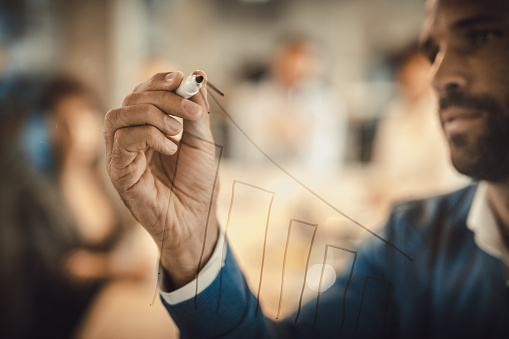 Close up of a businessman drawing diagram of progress on a glass wall.