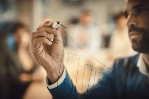 Photo of Close up f businessman drawing progress graph on transparent wipe board.