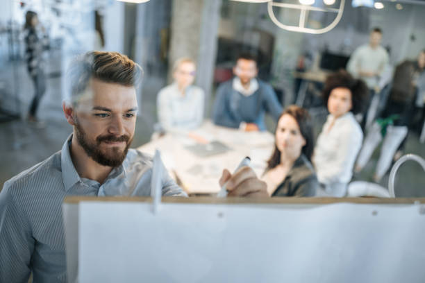 Young businessman writing ideas on whiteboard during a meeting with his colleagues.