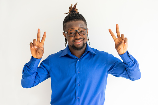 Cheerful handsome hipster black guy showing peace signs and looking at camera. Jolly positive peaceful young man in eyeglasses showing two hands with victory gesture. Winning concept