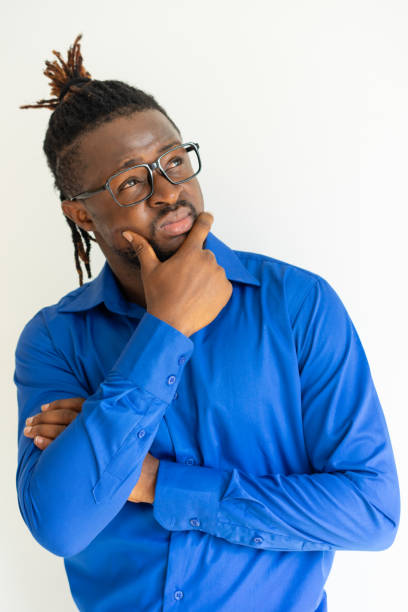 Pensive concentrated handsome young man looking up Pensive concentrated handsome young man looking up and rubbing chin. Thoughtful African businessman in glasses contemplating. Dilemma concept business person one man only blue standing stock pictures, royalty-free photos & images