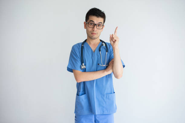 istock Serious young male doctor pointing upwards and looking at camera 956400768