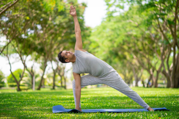 Inspired Indian man doing yoga asanas in city park Inspired Indian man doing yoga asanas in city park. Young citizen exercising outside and standing in yoga side angle pose. Fitness outdoors and life balance concept good posture stock pictures, royalty-free photos & images