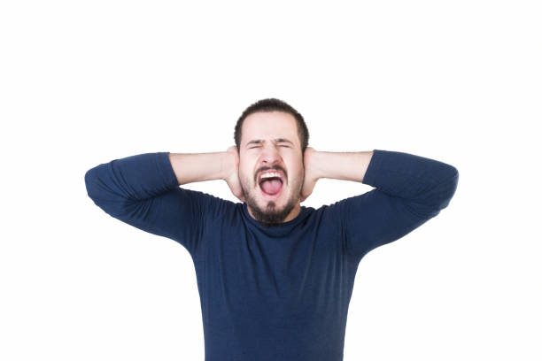 Portrait of furious young man screaming by covering his ears on a white background Portrait of furious young man screaming by covering his ears on a white background. Horizontal composition. Studio shot. man closing ears photos stock pictures, royalty-free photos & images