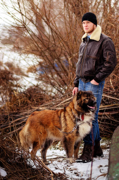 istock a young man in winter stands together with a Caucasian shepherd 956410394