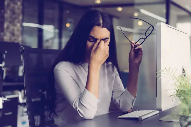 Photo of Depressed businesswoman rubbing eyes in office