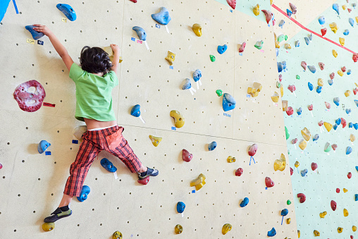 A 4 years old caucasian girl climbing on a gym climbing wall.