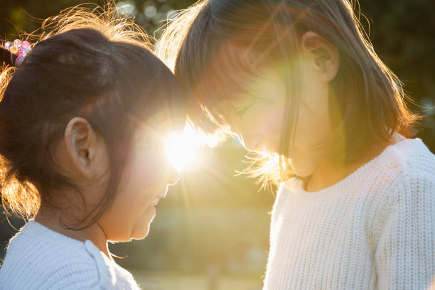 Sisters putting heads together and smiling outside with backlight