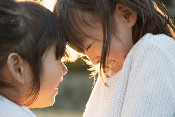 istock Sisters putting heads together and smiling outside with backlight 956421138