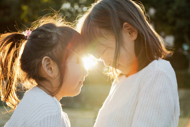istock Sisters putting heads together and smiling outside with backlight 956421156