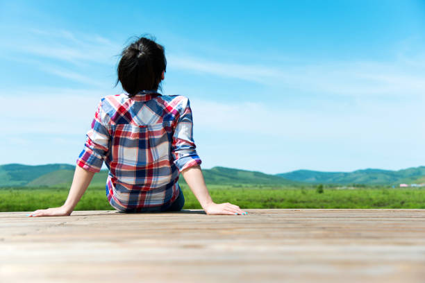 istock Woman looking away while sitting on wooden platform 956435326
