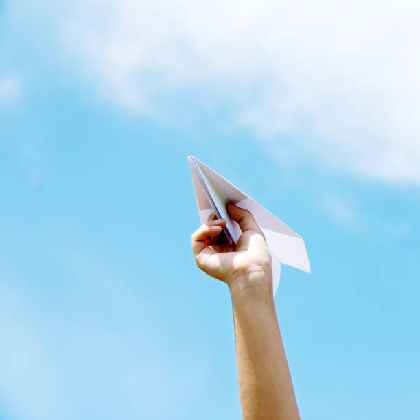 istock Boy hand holding a paper plane against the sky background 956436594