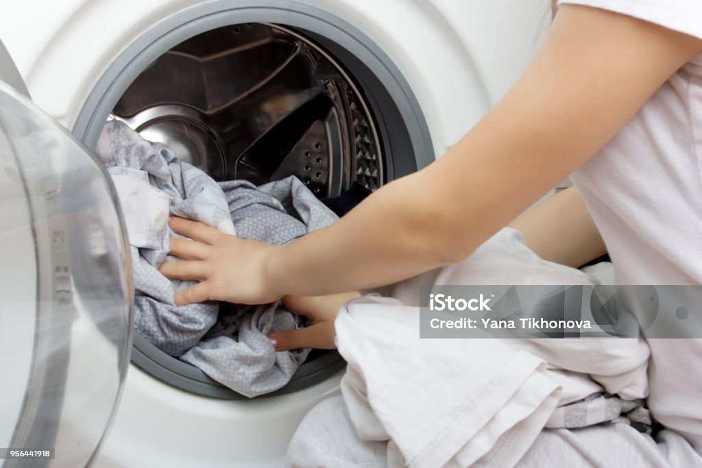 mains d’une jeune fille mettent les vêtements dans le tambour de la machine à laver - Photo de Lessive - Corvée domestique libre de droits