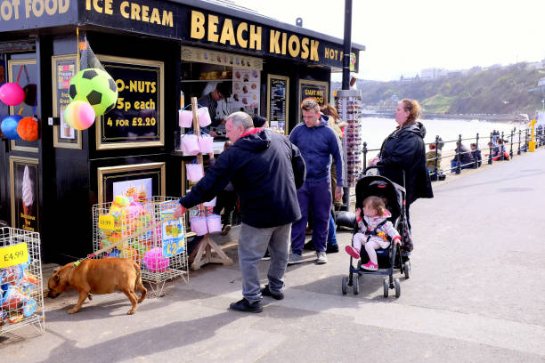 Scarborough, Yorkshire, UK. April 28, 2018.  Holidayamkers browsing the beach kiosk and sitting on the beach wall at Scarborough in North Yorkshire, UK.
