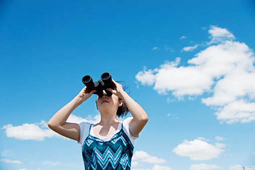 A woman looks at the sky with a binoculars