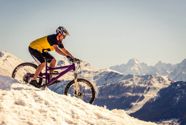 Mountain biker riding on the snow A male mountain biker riding down a ski slope in the Swiss alps adventure resort of Verbier, Switzerland. sports photography stock pictures, royalty-free photos & images