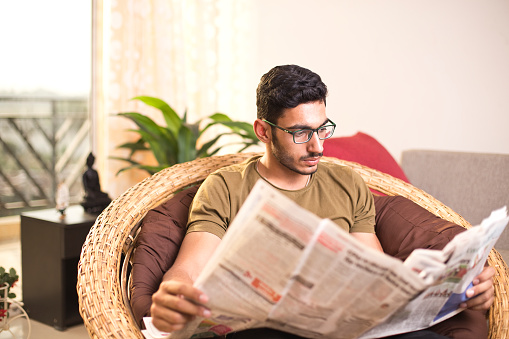 Young man reading newspaper at home