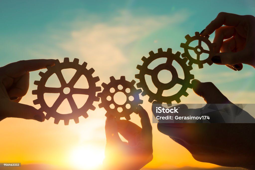 four gears in hands four gears in hands on a sunset background. teamwork. Teamwork Stock Photo