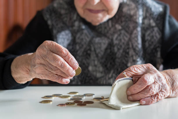 Elderly woman sitting at the table counting money in her wallet. stock photo