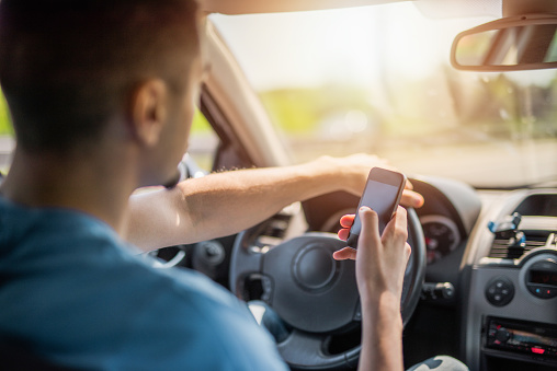 Careless young man texting a message while driving a car.
