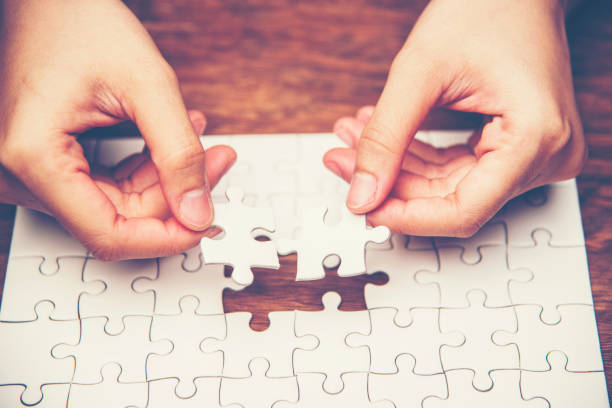 istock Cropped Hands Playing Jigsaw Puzzle On Wooden Table 956496536