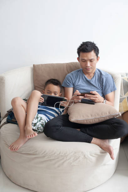 istock Malay father on phone while young son is on tablet 956496560