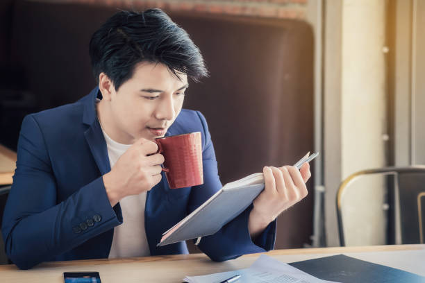 istock Businessman Reading Book While Having Coffee At Office 956499362