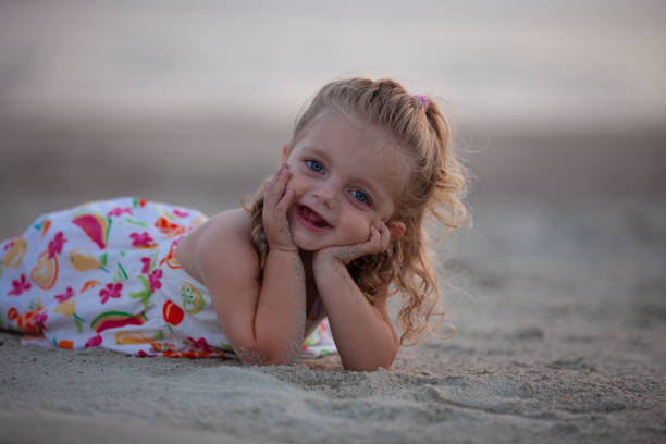 Portrait. Young blonde girl smiles as she lies on the beach at sunset.  bald head island stock pictures, royalty-free photos & images